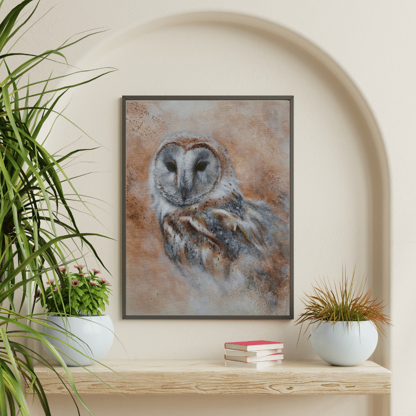 A framed art print of a barn owl with a textured, painterly background in earthy brown, gray, and white tones, displayed on a wooden shelf in a styled interior setting with potted plants.