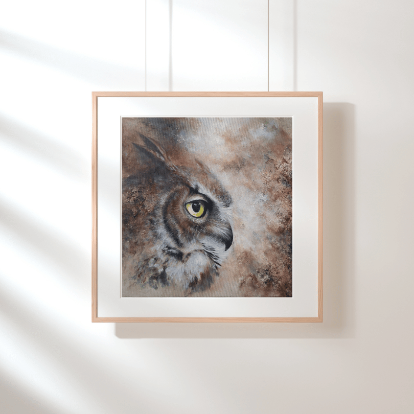 Framed owl portrait wall art hanging on a white wall, with a light wood frame, white mat, and a textured painting showing the owl's face in brown, gray, and cream tones with a yellow eye.